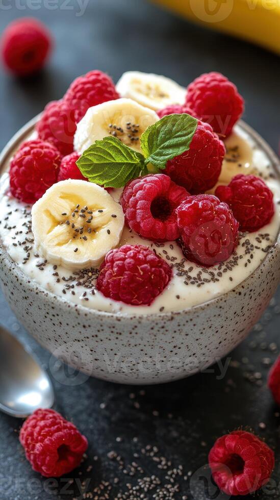Delicious bowl of yogurt topped with bananas, raspberries, and chia seeds on a dark surface photo