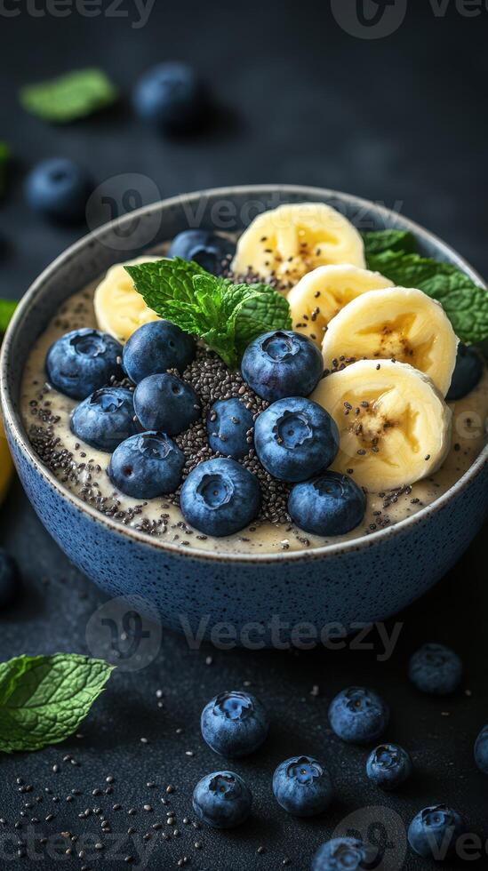 Delicious smoothie bowl topped with blueberries, banana slices, and mint leaves on a dark background photo