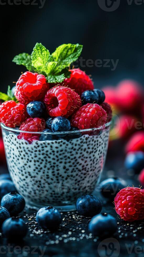Chia seed pudding topped with fresh raspberries and blueberries in a glass bowl on a dark backdrop photo