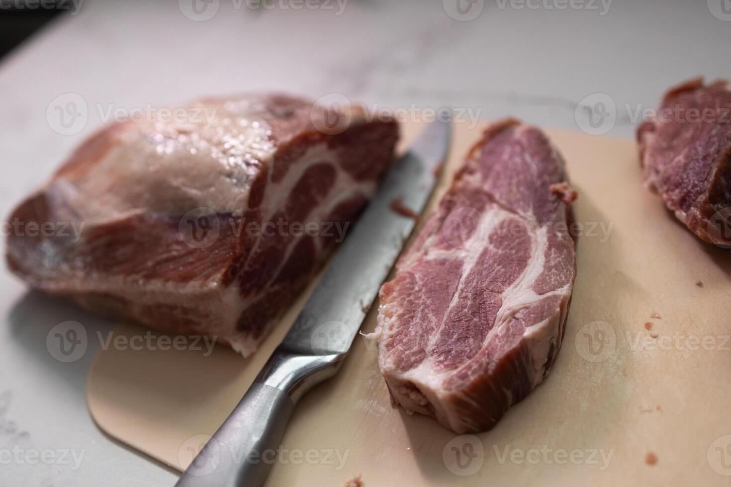 A Freshly Cut Pork Shoulder with a Sharp Knife Resting on the Countertop in the Kitchen photo