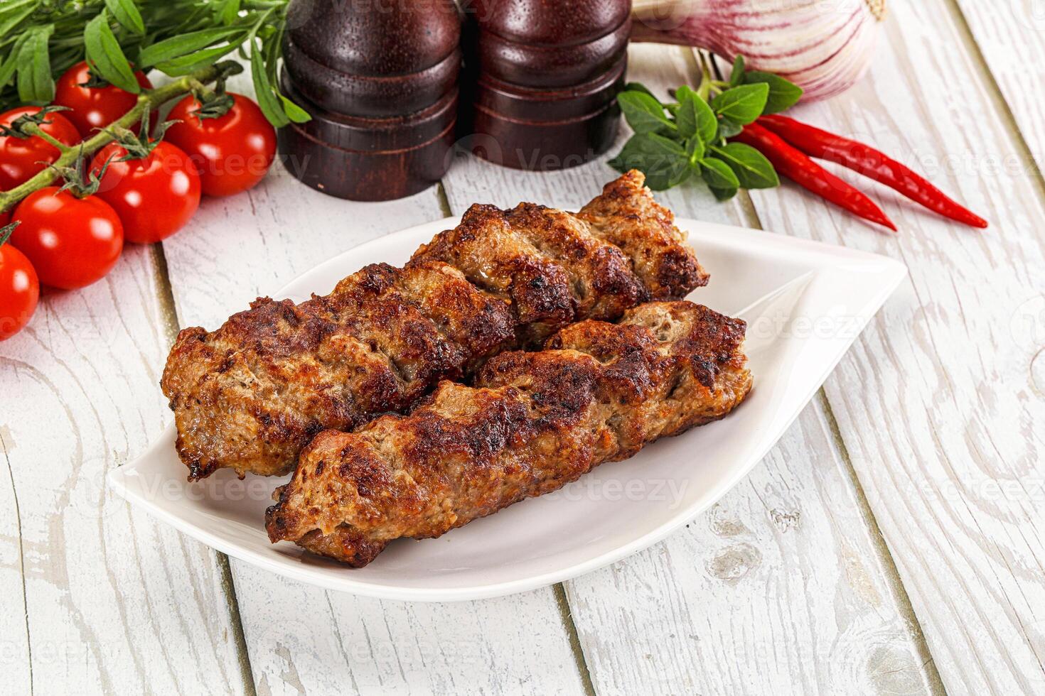 Two meat skewers on a white plate with tomatoes and herbs photo