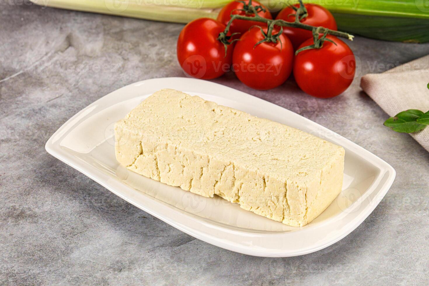 A piece of cheese on a plate next to tomatoes and other vegetables photo