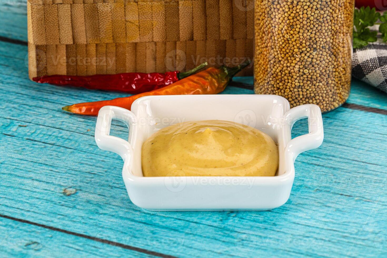 A bowl of mustard with a wooden spoon and a bottle of mustard photo