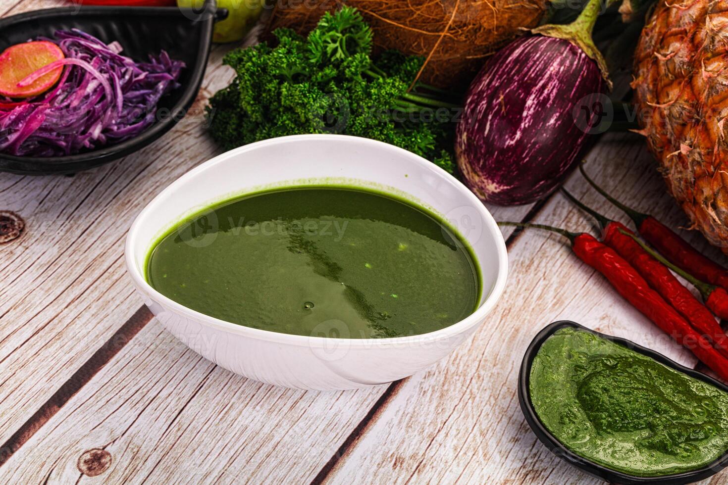 A bowl of green sauce on a table with other ingredients photo