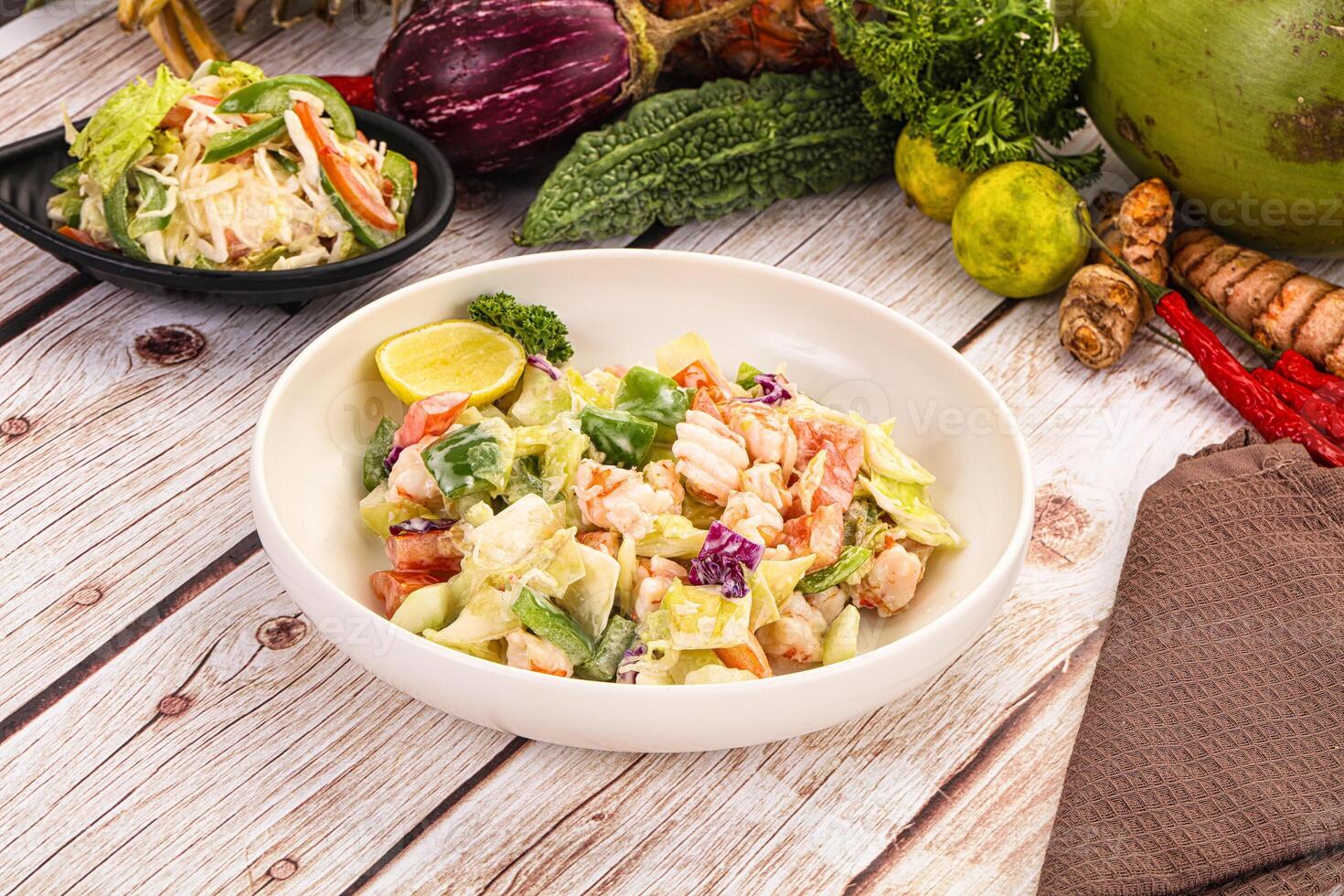 A bowl of salad on a table next to a bowl of fruit photo