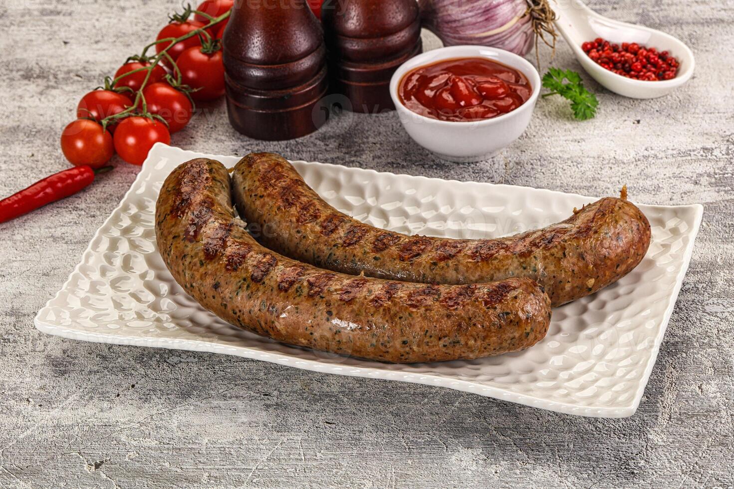 Two sausages on a white plate with tomatoes and ketchup photo
