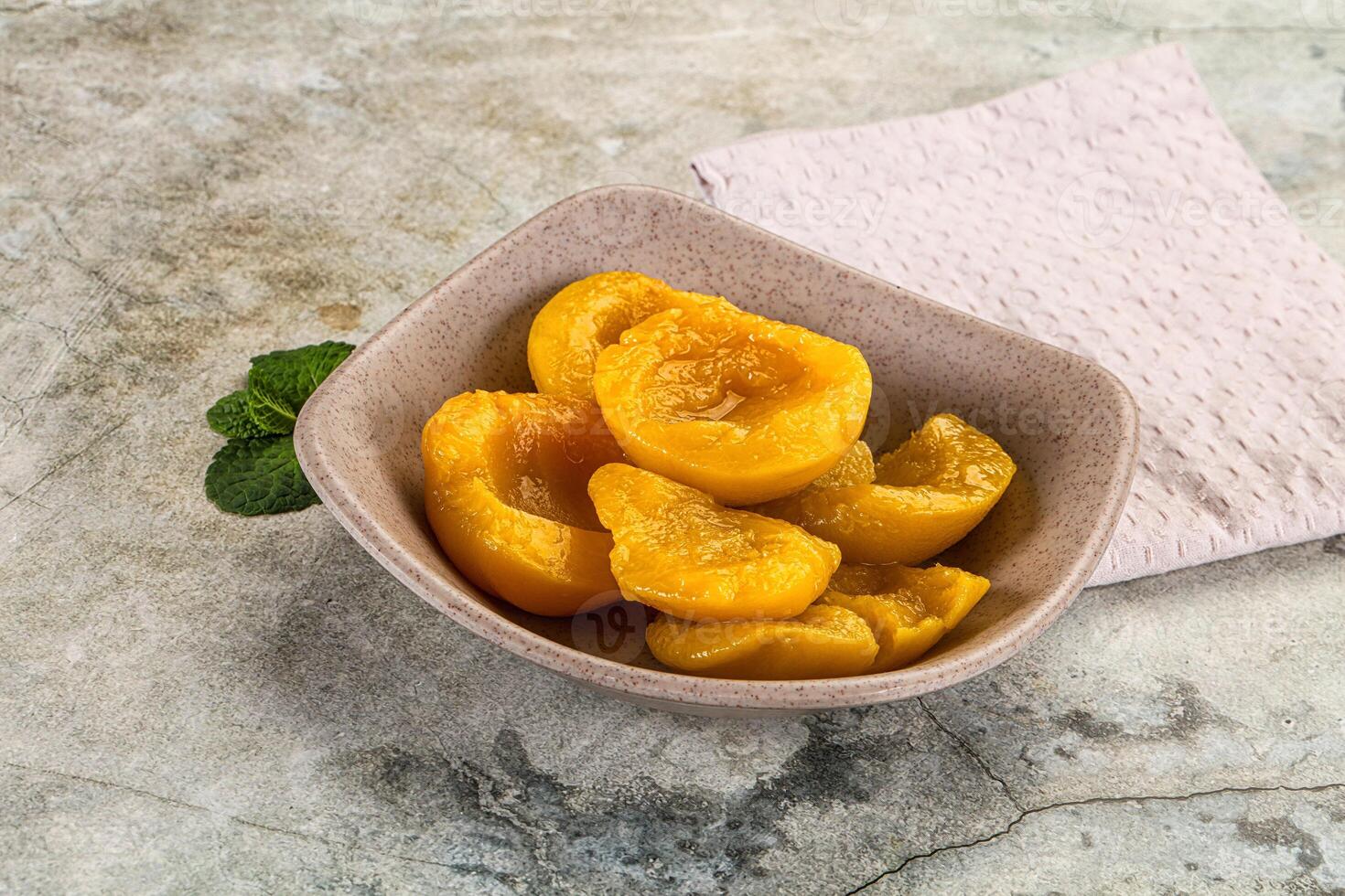 A bowl of yellow peaches sitting on a table photo