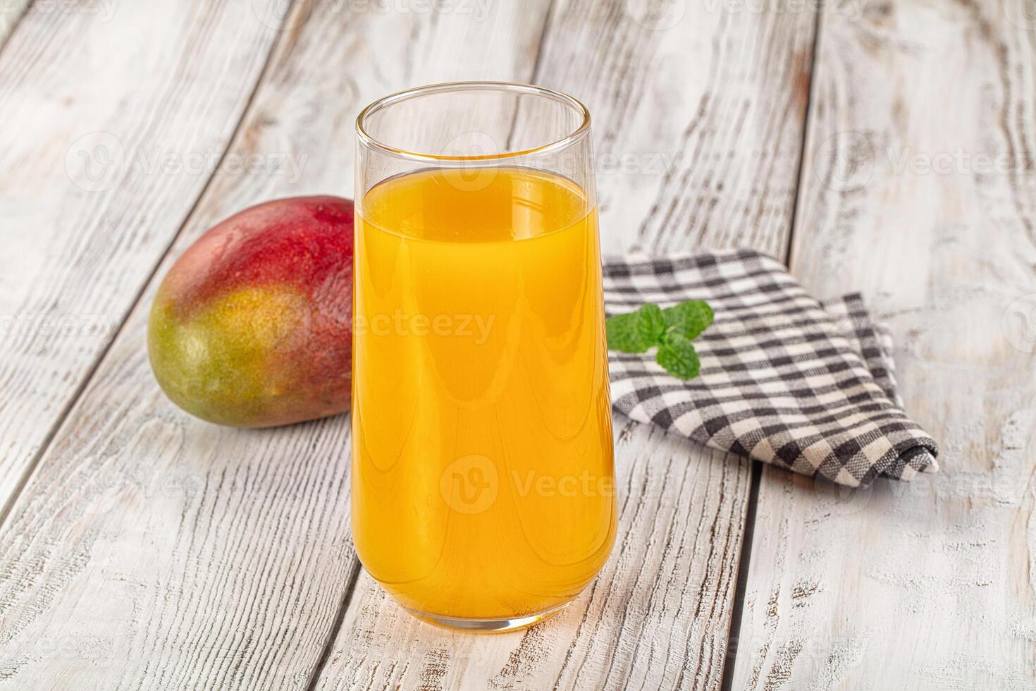 A glass of orange juice with a mango on a wooden table photo