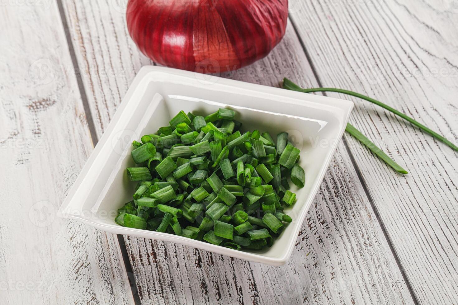 A bowl of chopped green onions and a red onion photo