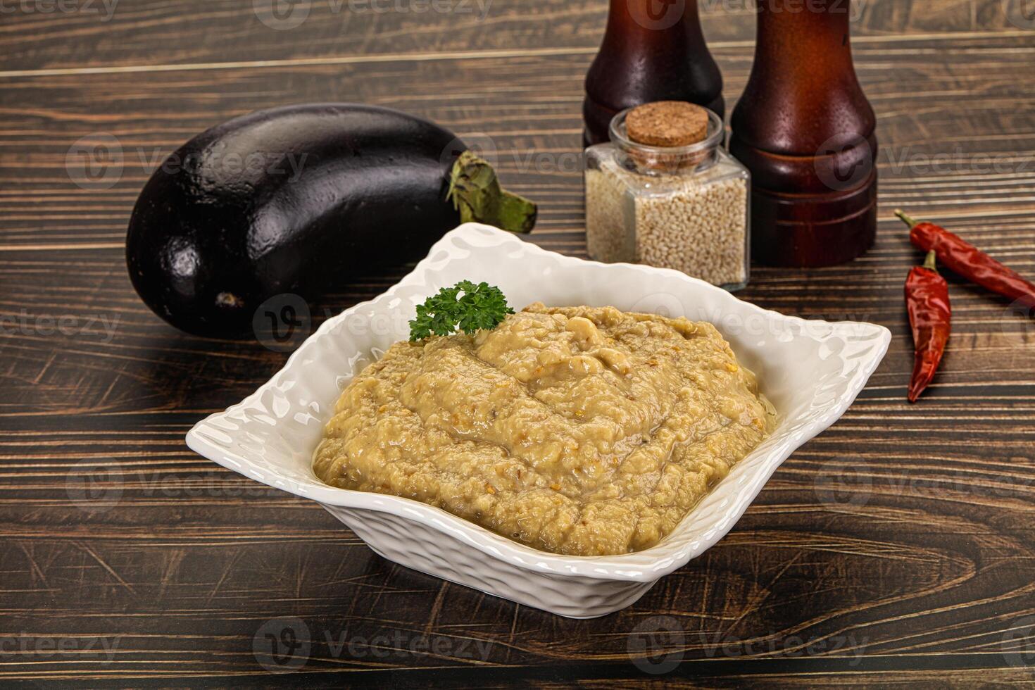 A bowl of eggplant dip with a pepper and a bottle of hot sauce photo