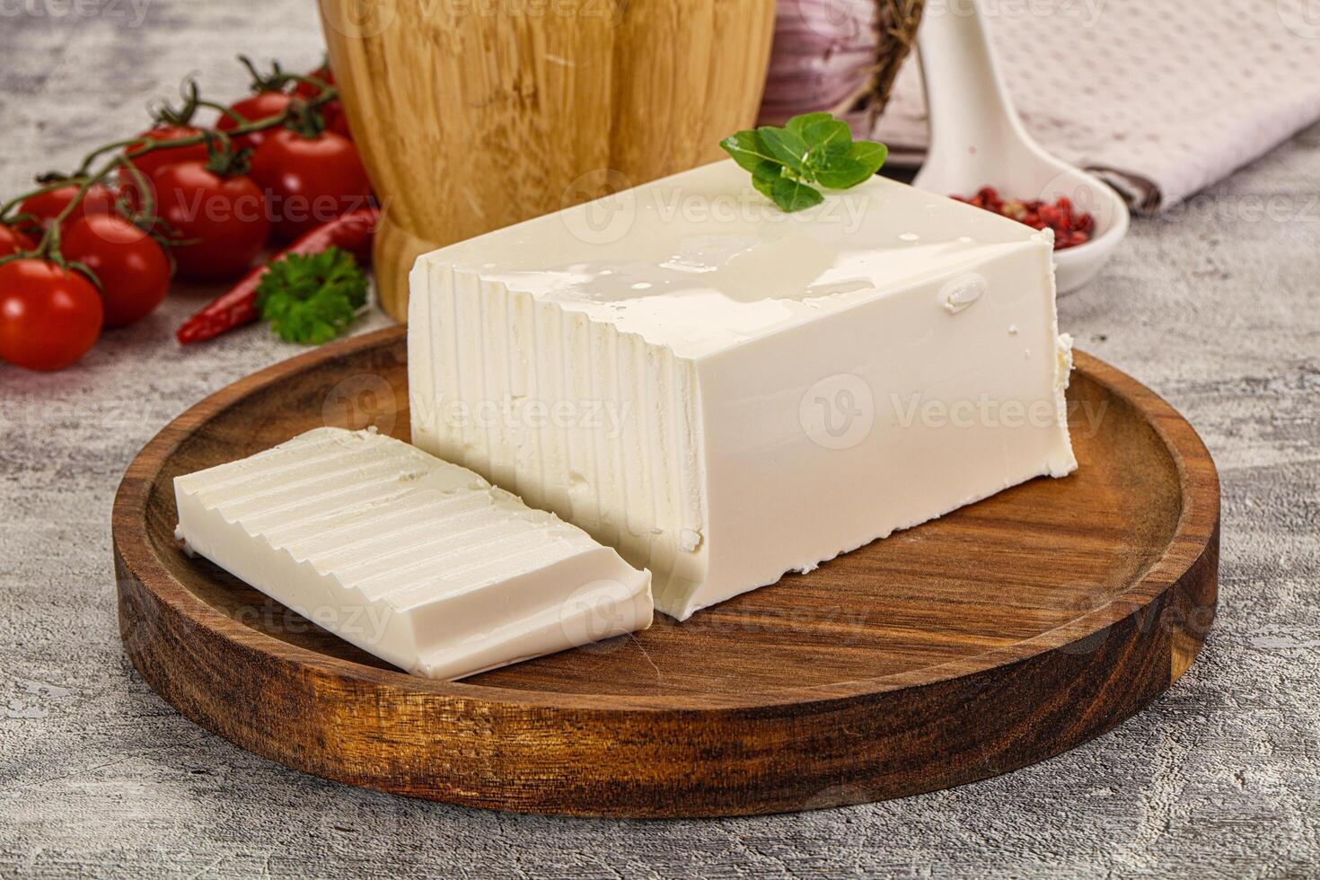 A piece of cheese on a wooden plate with tomatoes and herbs photo