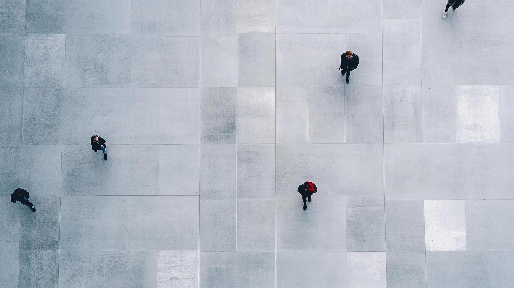Overhead view of people walking on a tiled floor. People are spread apart and look tiny. Tiled floor is made of large square tiles. photo