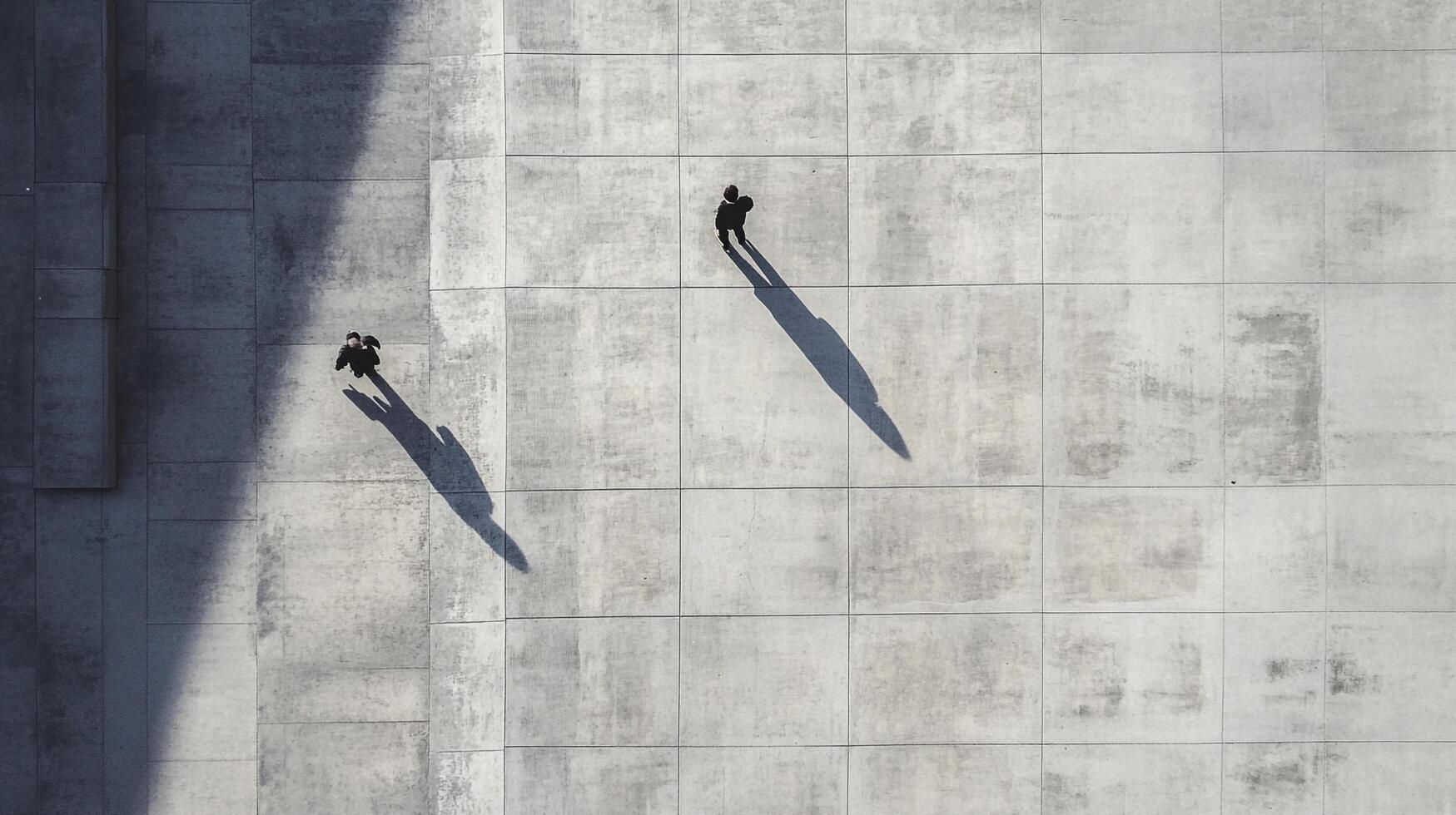 Overhead shot of two anonymous figures walking along a concrete surface, their shadows stretching beside them, creating contrast. photo