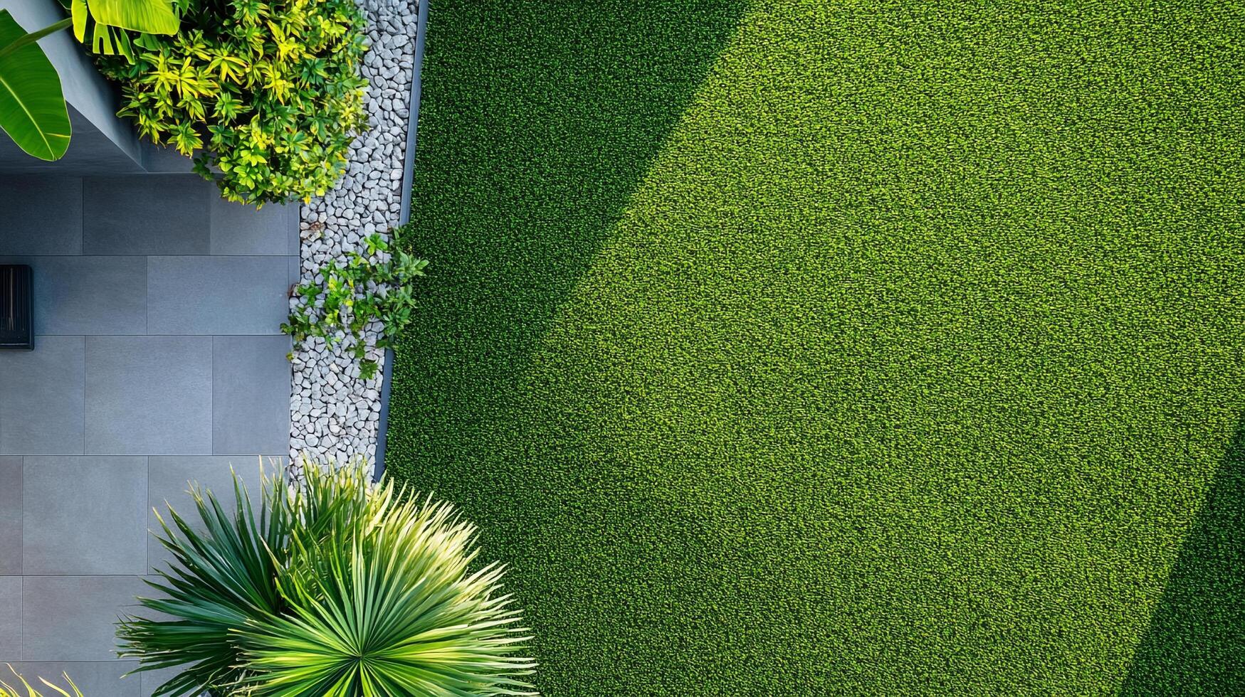Overhead shot showcasing a manicured garden with vibrant green artificial turf, textured stone path, and lush tropical plants in a modern setting. photo