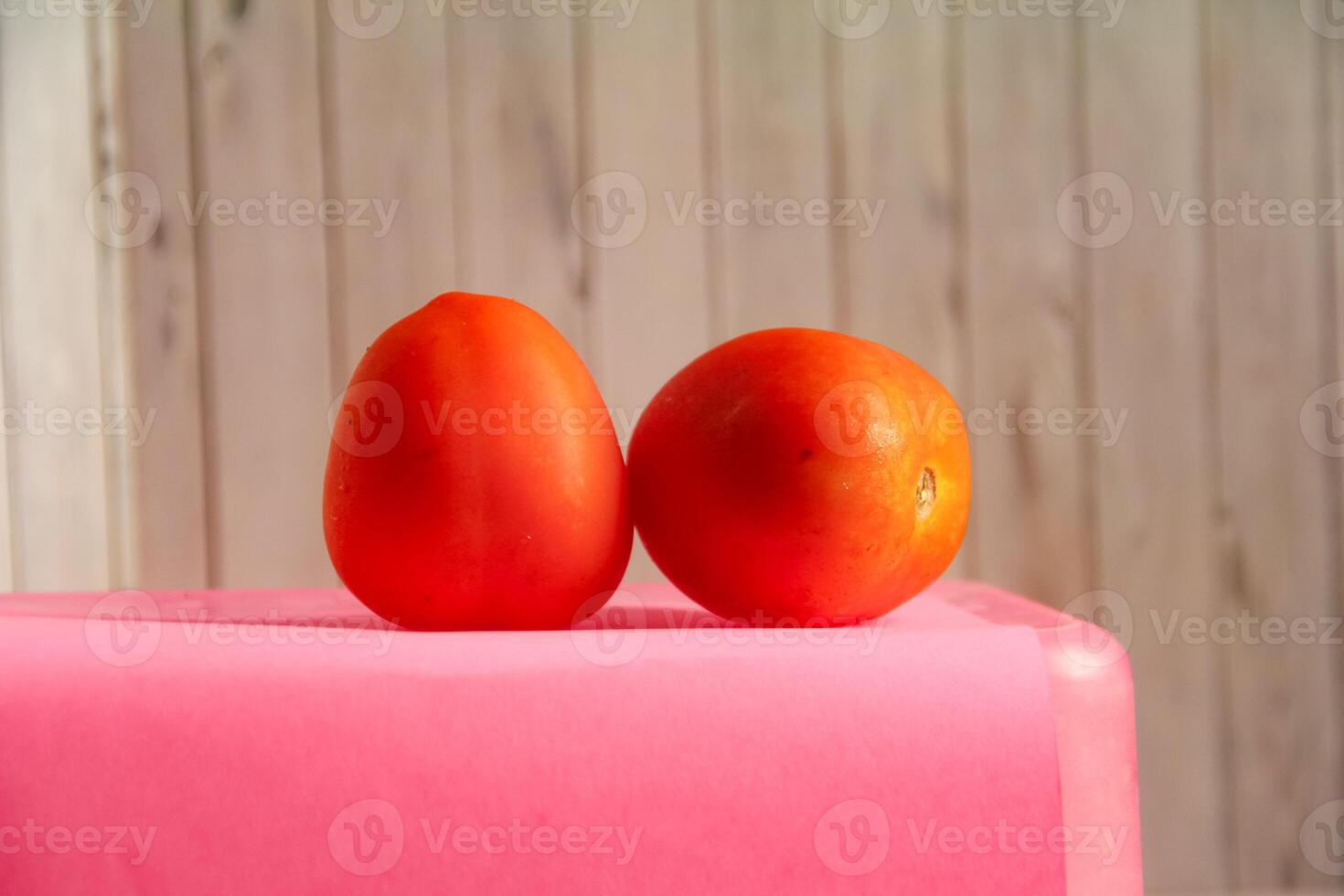 Two tomatoes on a pink table photo