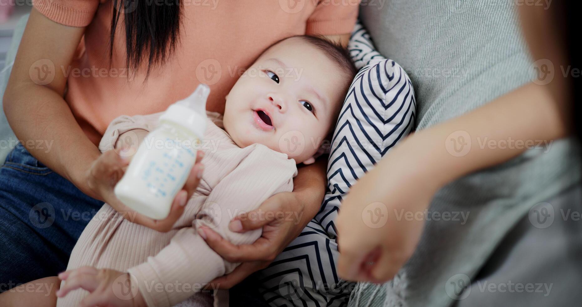 Sister is having fun with her little brother while drinking milk in her mother's arms on the sofa in the cozy living room. photo