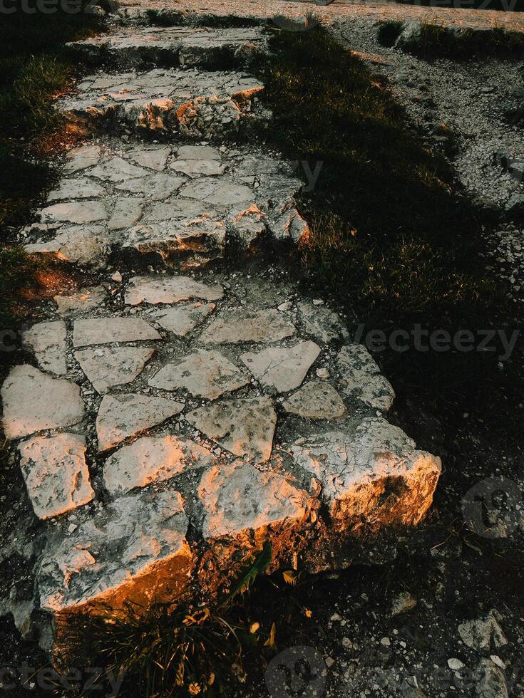 Stone paved path illuminated by golden sunset light. Warm sunlight illuminating a stone paved path with grass growing in between the slabs, evoking a sense of tranquility and the beauty of nature photo