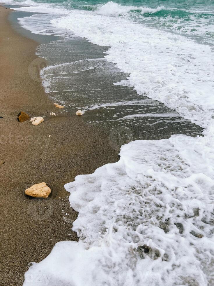 Sea waves crashing on sandy beach creating white foam. Gentle waves washing onto sandy beach, creating soothing white foam, forming peaceful coastal scene perfect for relaxation and tranquility photo