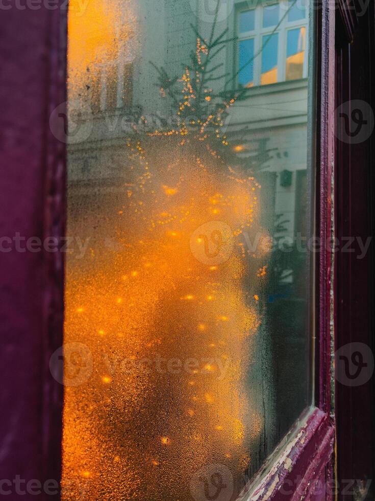 Christmas tree with lights reflecting on foggy window during winter. Warm orange Christmas lights reflecting foggy window, cozy and festive atmosphere, cold winter day, sense of magic and celebration photo