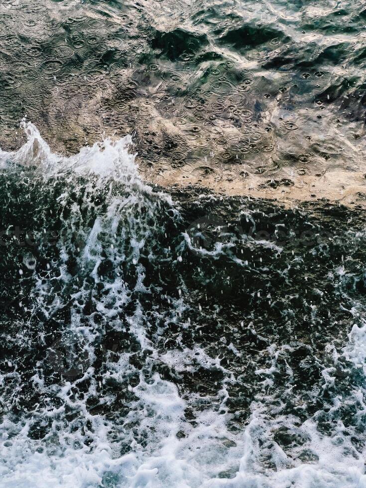 Rain falling on dark ocean water with white foam waves crashing. ocean waters creates captivating scene, with white foam waves crashing against shore, showcasing beauty of nature's rhythmic dance photo