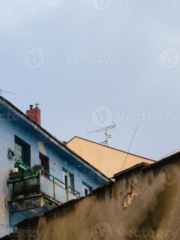 Old, colorful, weathered buildings with balconies. Low angle view of weathered buildings with balconies, antennas, and chimneys against a cloudy sky, showcasing urban decay and architectural details photo