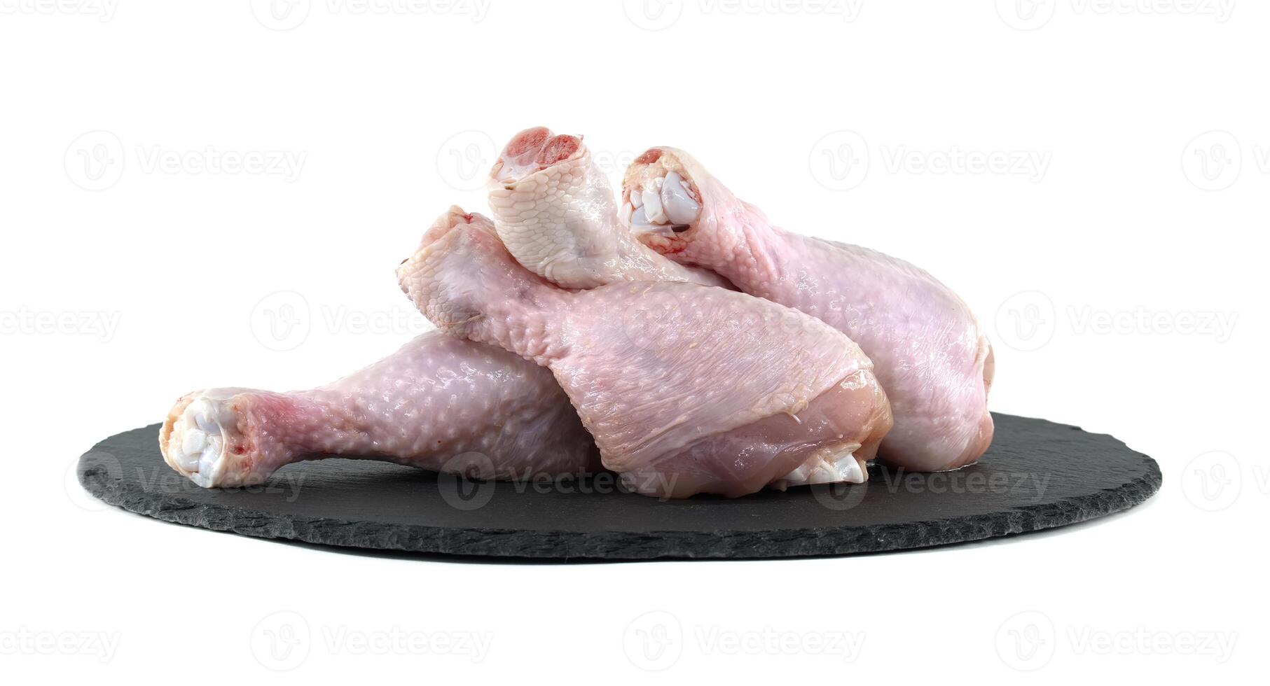 Raw chicken drumsticks resting on a black slate cutting board photo