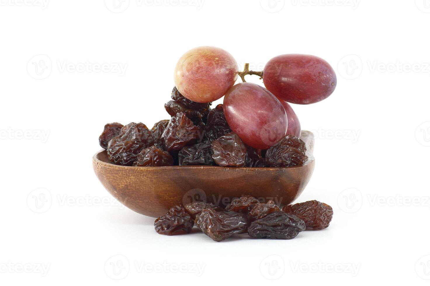 Small wooden bowl brimming with dark raisins and bunch of ripe red grapes sits on a white background photo