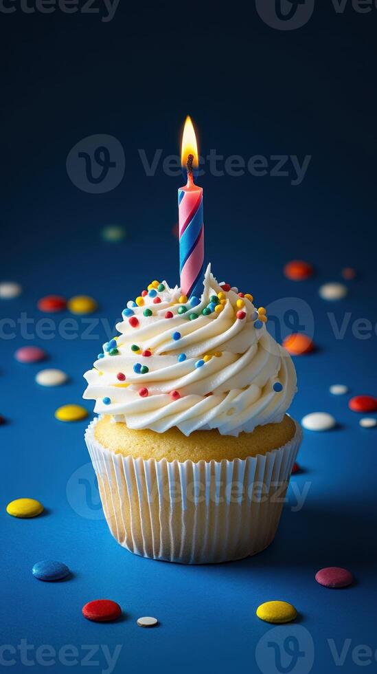Birthday cupcake with colorful frosting and candle against a blue background surrounded by candy photo