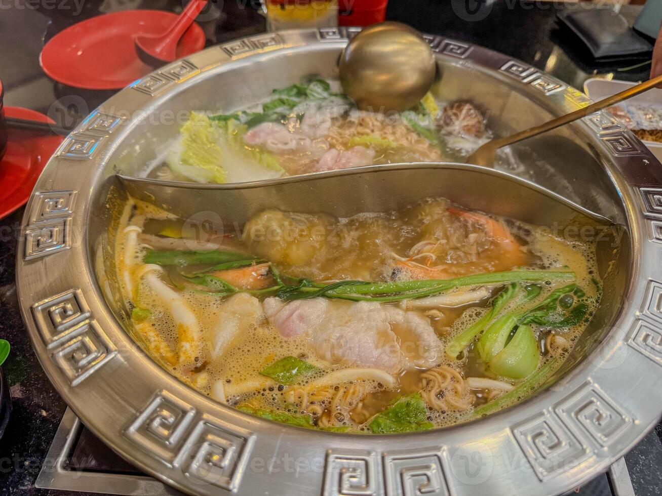 Steaming hot pot filled with vegetables and seafood at a busy diner setting photo