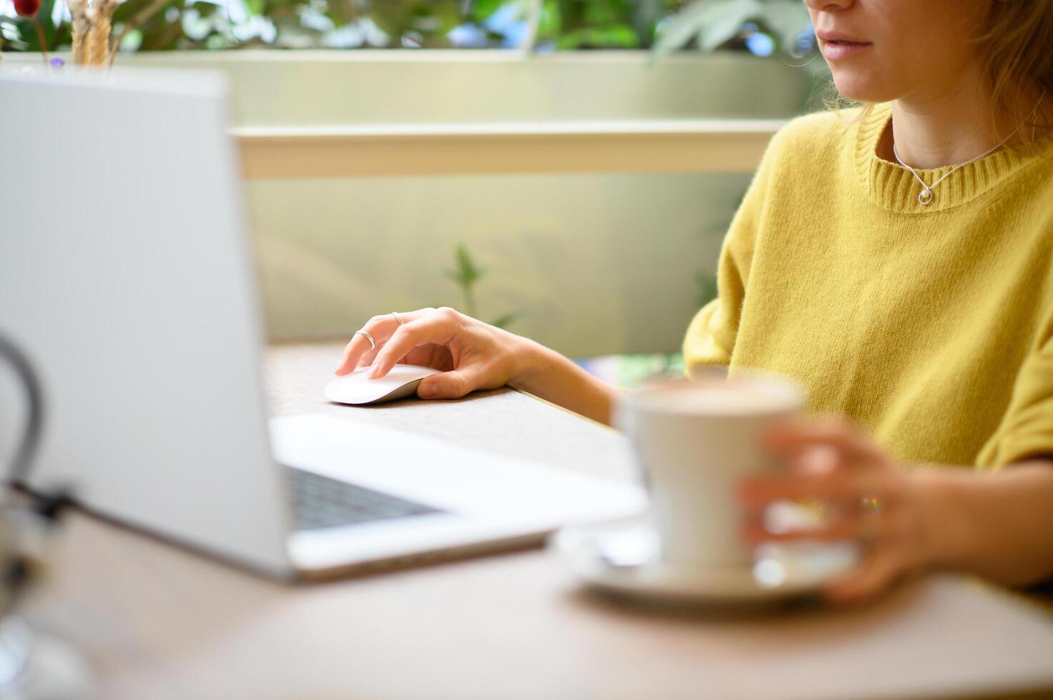 A freelance worker balances productivity and relaxation, holding coffee while working on her laptop in a modern cafe. photo