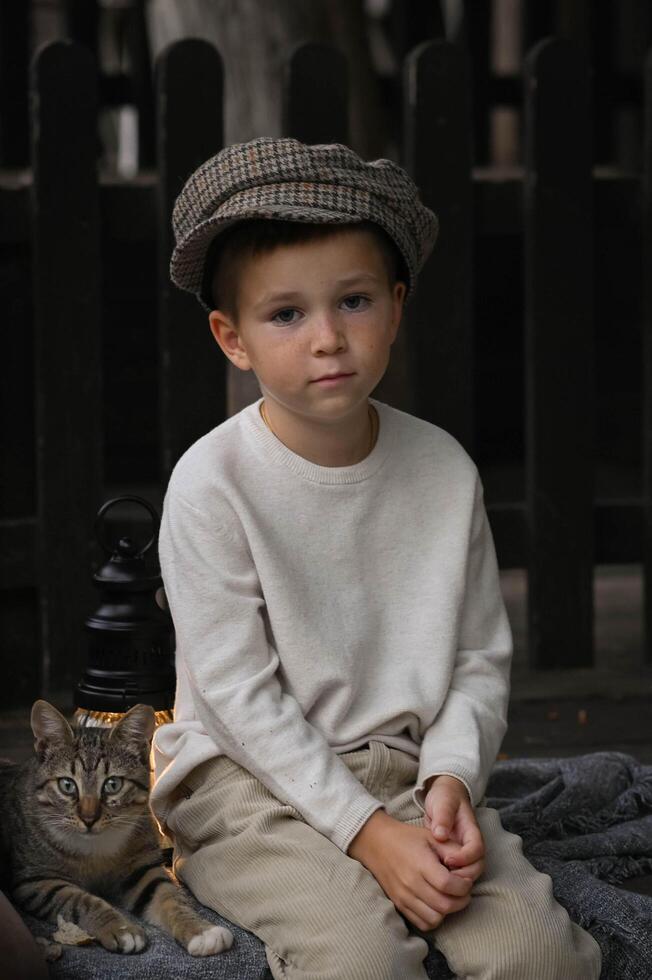 A young boy wearing a vintage cap holds a cat in his arms, his eyes full of warmth and curiosity. The soft, natural light highlights the texture of his hat and the cats fur. photo