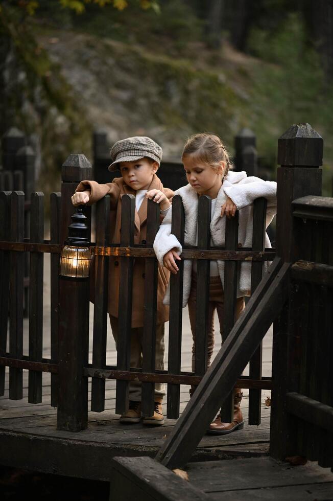 dressed in old fashioned clothes a boy and girl stand on a rustic wooden bridge with a light in hands photo