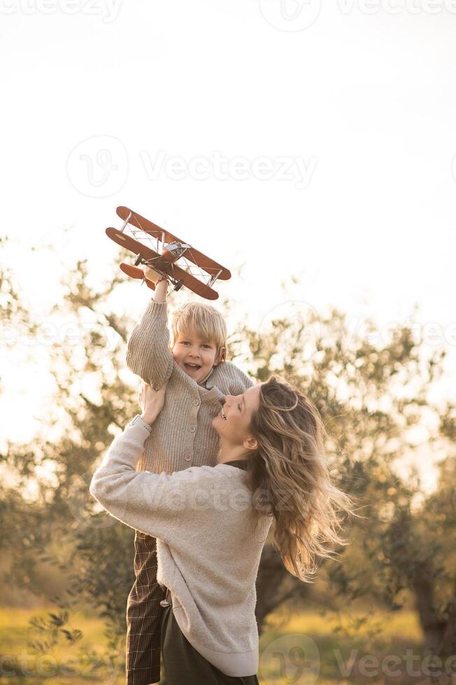 As the sun sets, a mother and son run through a field, guiding a toy plane through the air. photo