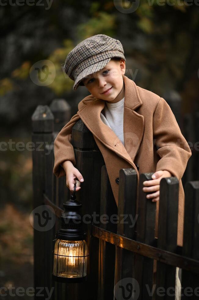 A boy in a vintage coat and hat holds a lantern, his face illuminated by its warm glow as darkness gathers around him. photo