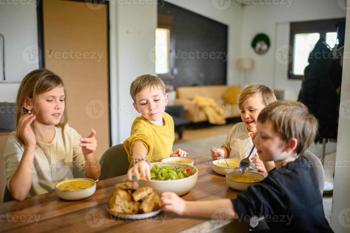 The children happily eat soup, with a bright and healthy salad ready to be shared. photo