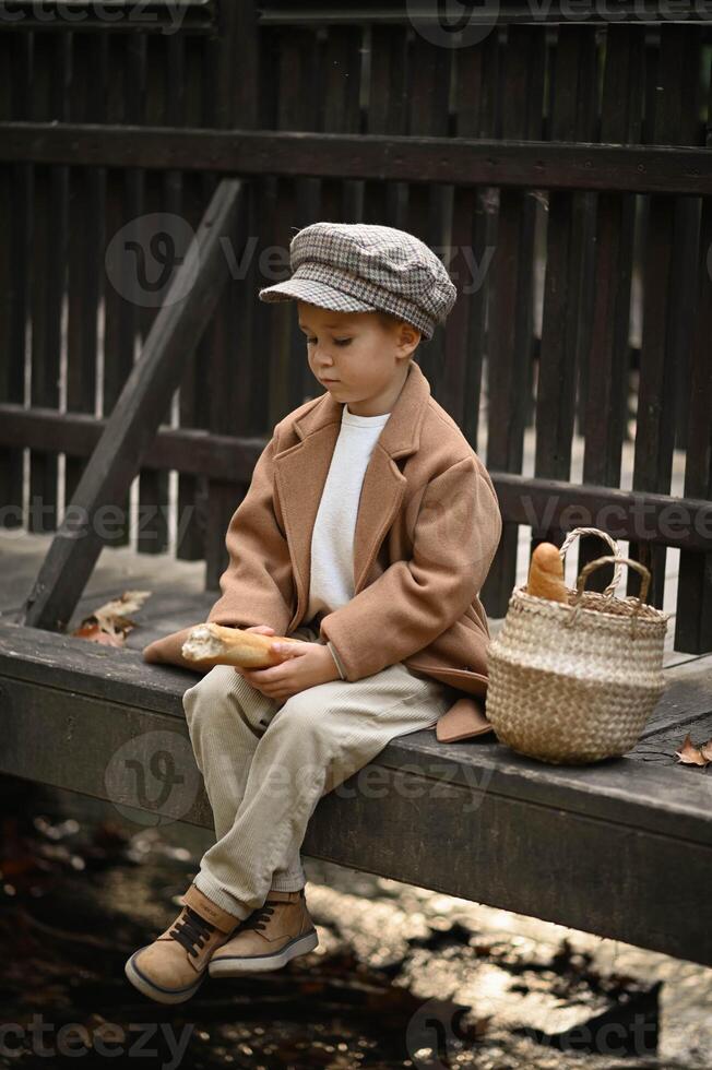 Dressed in old-fashioned clothes, a young boy carries a basket of fresh baguettes on a bridge, as if frozen in a timeless, nostalgic moment. photo