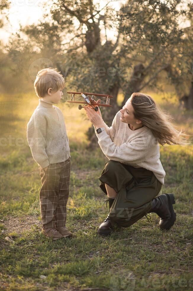 A mother and her son play with a toy airplane in a golden field at sunset, laughing together. photo