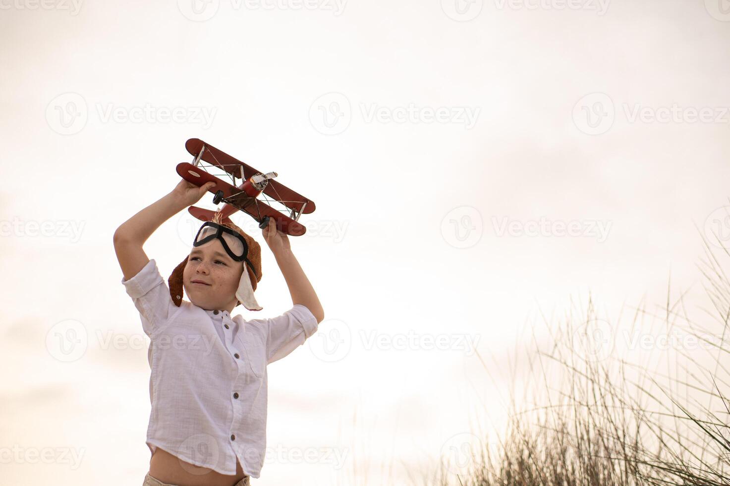 Standing against a golden sunset, the boy grips his toy plane tightly, his pilots cap adding to the magic of his imagined journey. photo