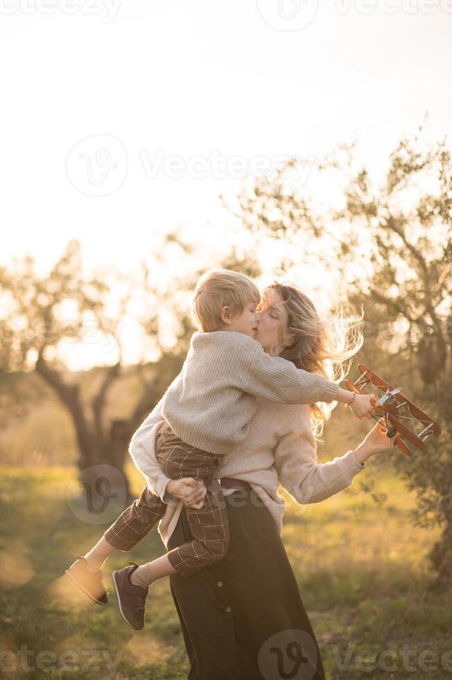A mother and her little boy chase dreams in a sunset-lit field, flying a toy plane with excitement. photo
