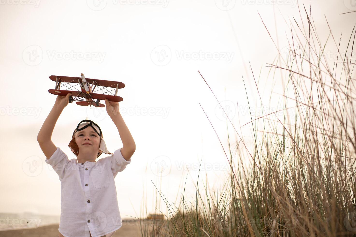 A young boy in a pilots hat holds a toy airplane high against the sunset sky, his eyes filled with dreams of adventure and flight. photo