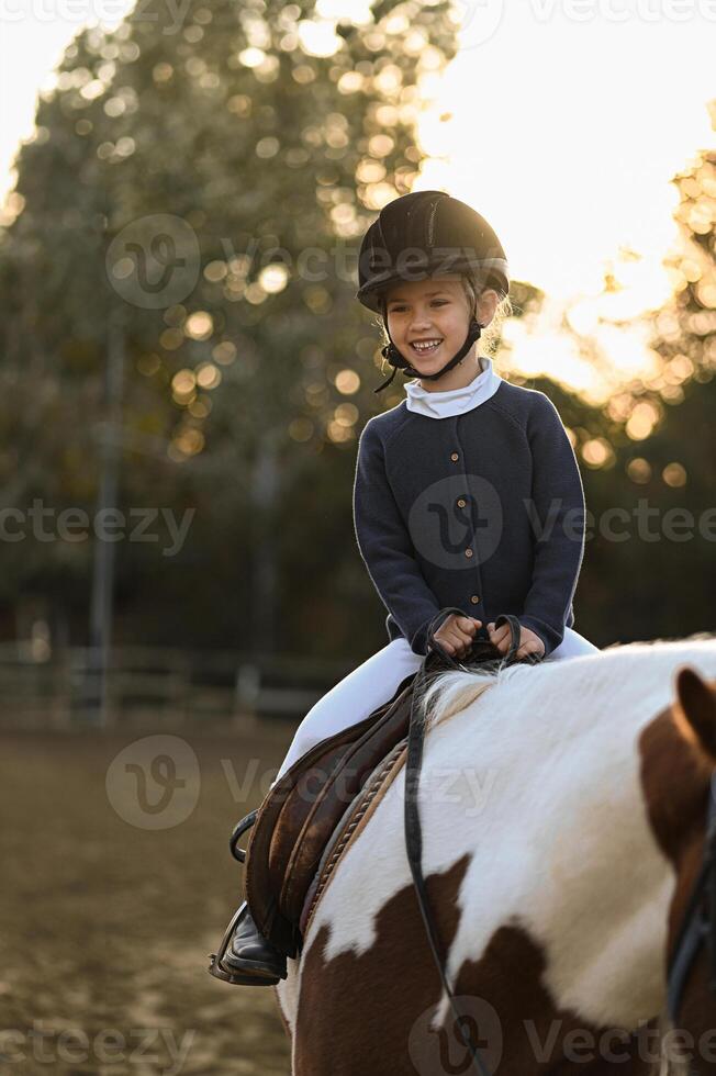 Silhouetted by the sunset, a girl on a spotted horse learns the art of horseback riding. photo