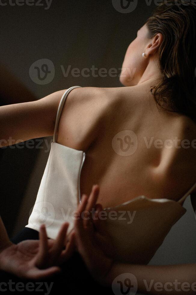 A young woman fastening a white corset on her back. photo