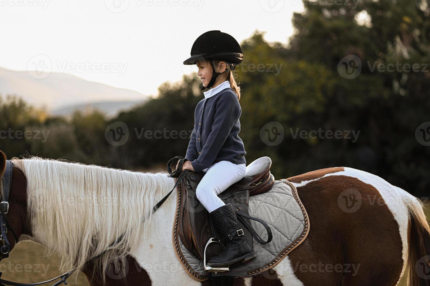 A gentle breeze rustles as a young rider gains confidence on her speckled horse at sundown. photo