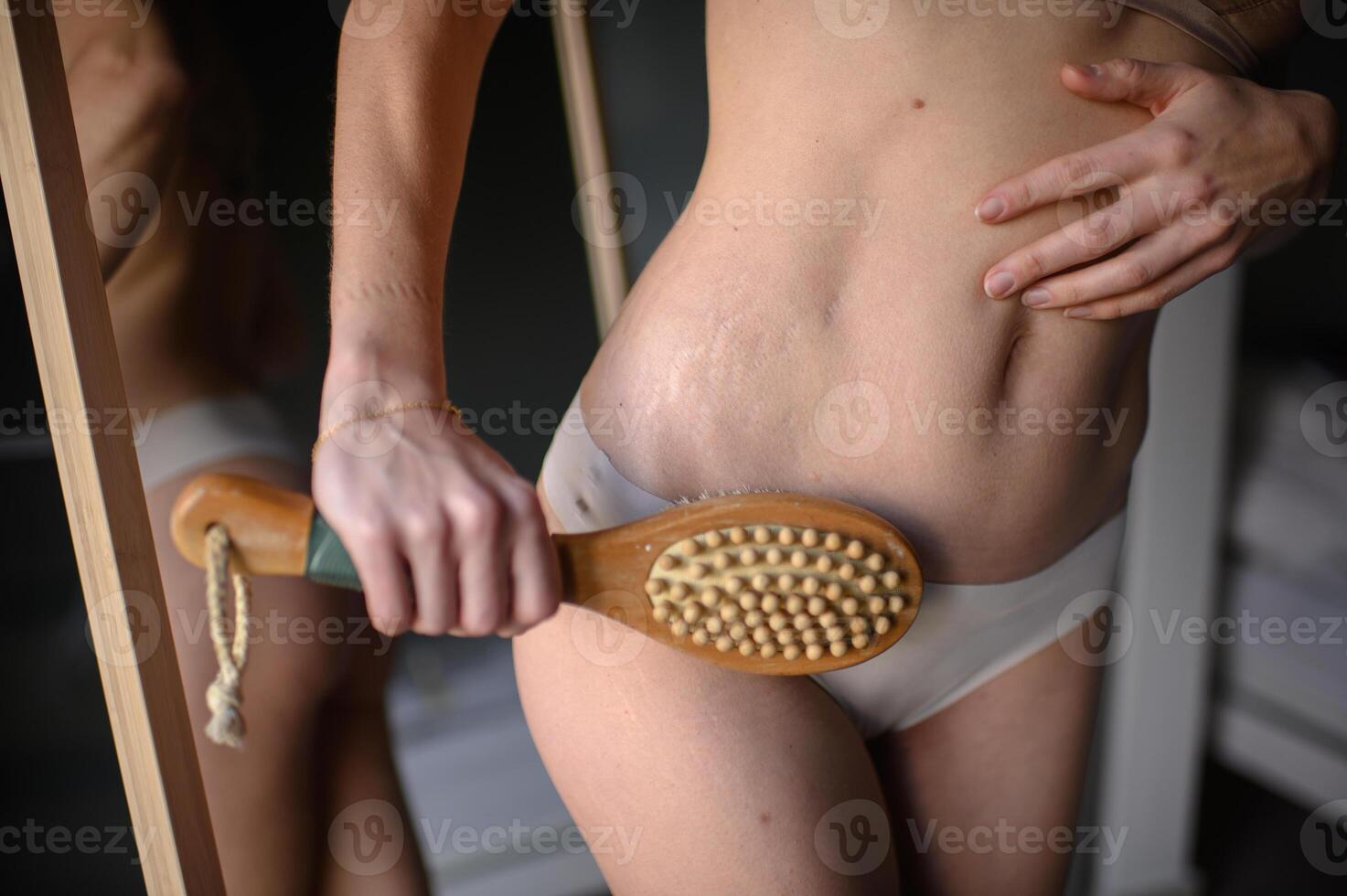 She looks at her reflection while gripping a wooden dry brush, ready to massage her skin. photo
