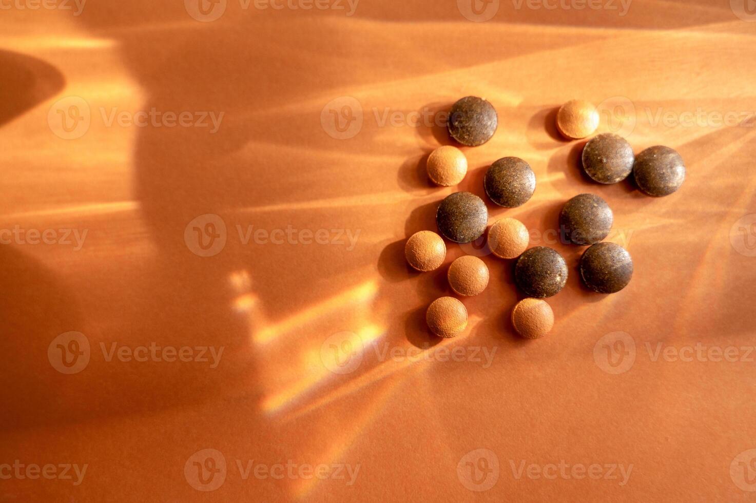 Medical supplements in the form of round tablets lie on an orange background. Tablets are round in shape. They are made of herbs of brown and orange color. Concept of natural medicine. photo