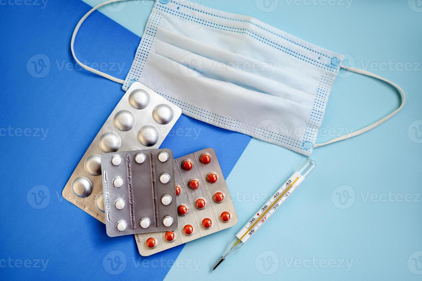 tablets in a blister, a medical mask and a thermometer on a blue background. three blisters of tablets photo