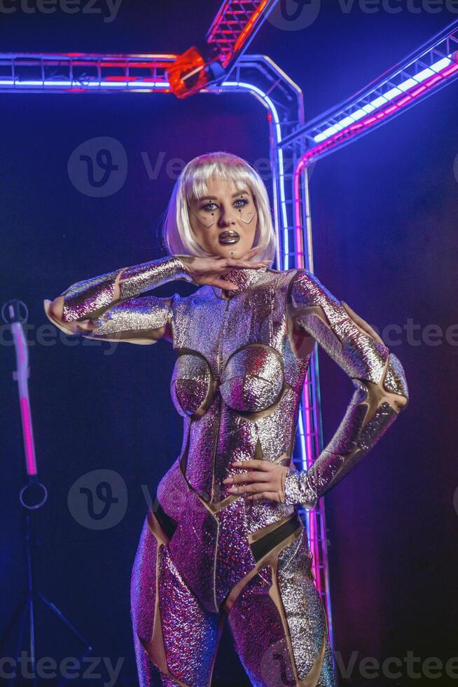 blonde girl as cyber robot. cyber girl in shining silver armor in neon. blonde with fantastic makeup and image in dark key and colored light. fashion model posing in cyber space. full body armor jumpsuit photo