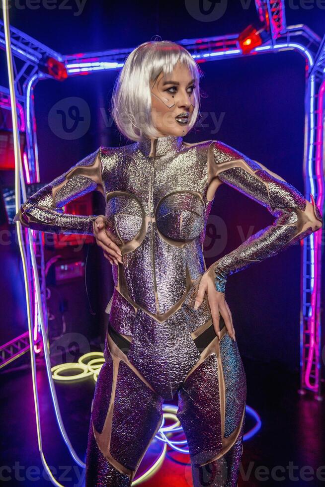 blonde as cyber robot. Girl in shining silver armor in neon. Blonde with fantastic makeup and image in dark key and color light, posing in cyberspace. screens and wires glow around. photo