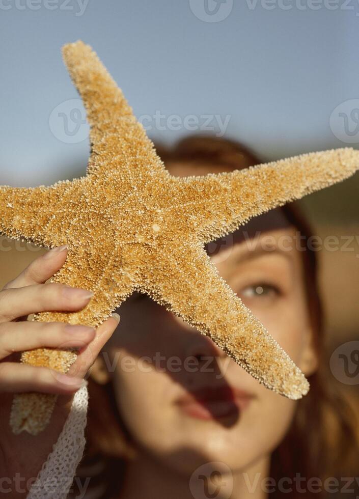 close up of beautiful young girl, starfish near her face, girl holding starfish near her face summer sea morning concept. focus on starfish photo