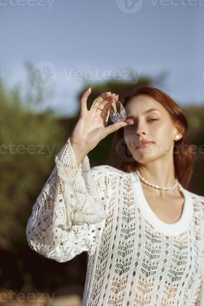 woman meditating on wild beach shore and holding crystal heart.close up of beautiful young girl on sea beach. she enjoys weather. near face holds crystal from crystal. concept of summer sea morning . photo
